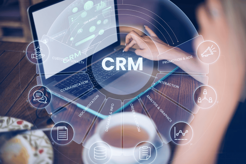 A imagem mostra uma pessoa usando um laptop em uma mesa, com uma xícara de café ao lado. Na tela do laptop, há gráficos e dados que sugerem o uso de um sistema de CRM (Customer Relationship Management). Em torno do laptop, há ícones que representam diferentes funções do CRM, como comunicação, análise, promoção e interação. O ambiente é acolhedor, com uma mesa de madeira e um prato visível, sugerindo um espaço de trabalho confortável. A imagem simboliza os benefícios do uso de CRM, uma estratégia de vendas pelo Whastapp